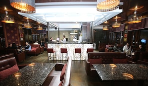 A restaurant with marble-topped tables and booths, a bar area, and pendant lighting.