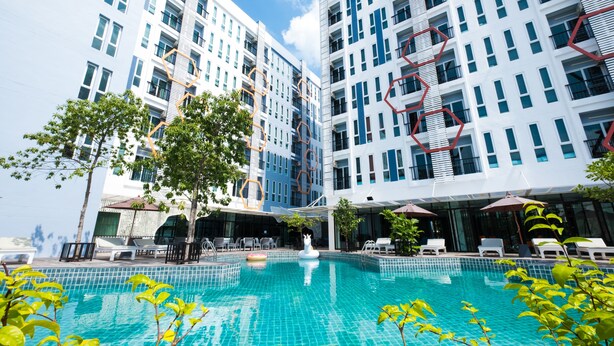 A modern hotel with a swimming pool, outdoor seating, and a view of the surrounding buildings. - P Plus Hotel (Pattaya)