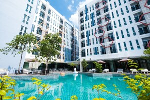 A modern hotel with a swimming pool, outdoor seating, and a view of the surrounding buildings.