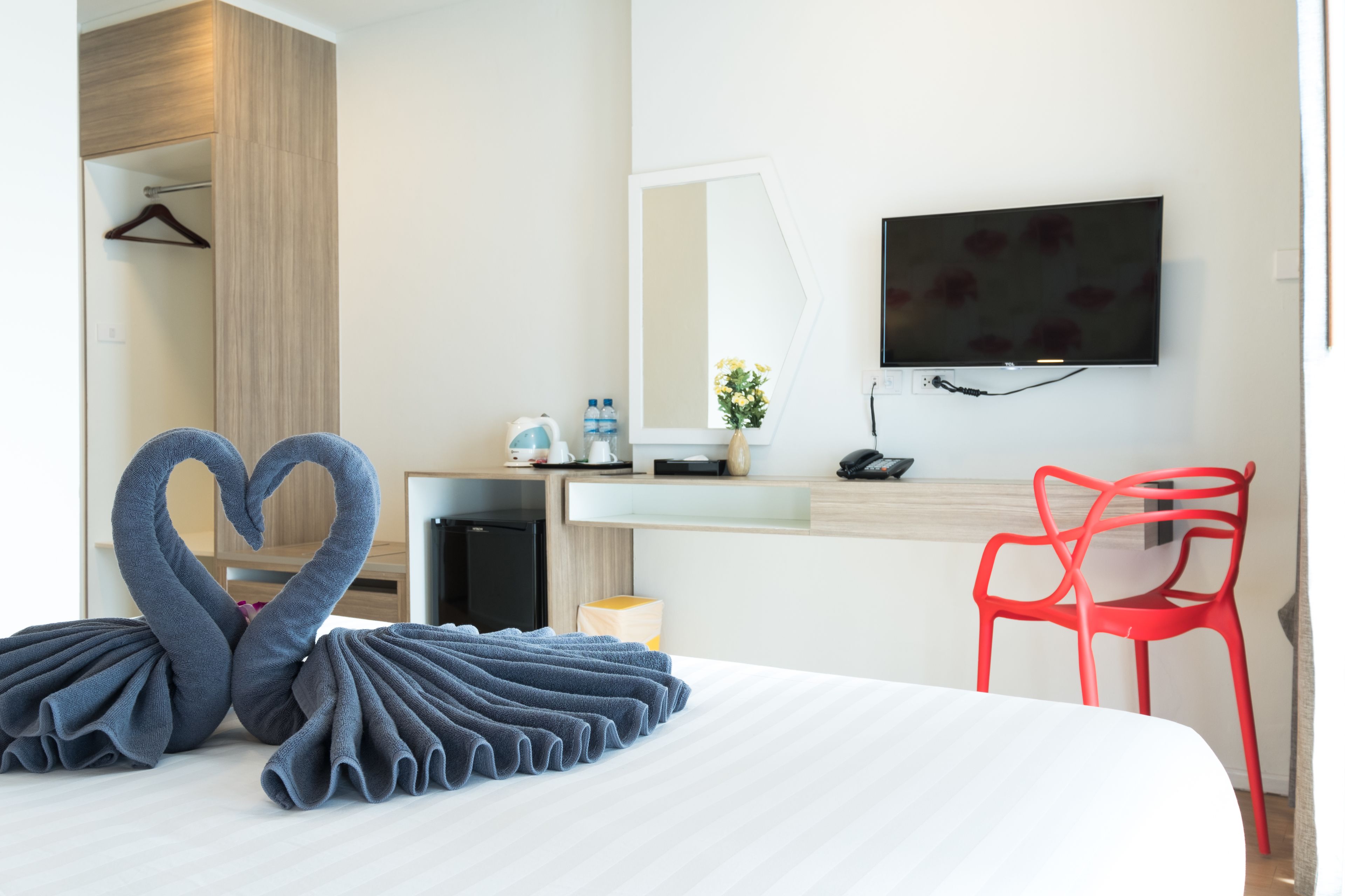 A hotel room with a bed, a TV, a desk, and a red chair.