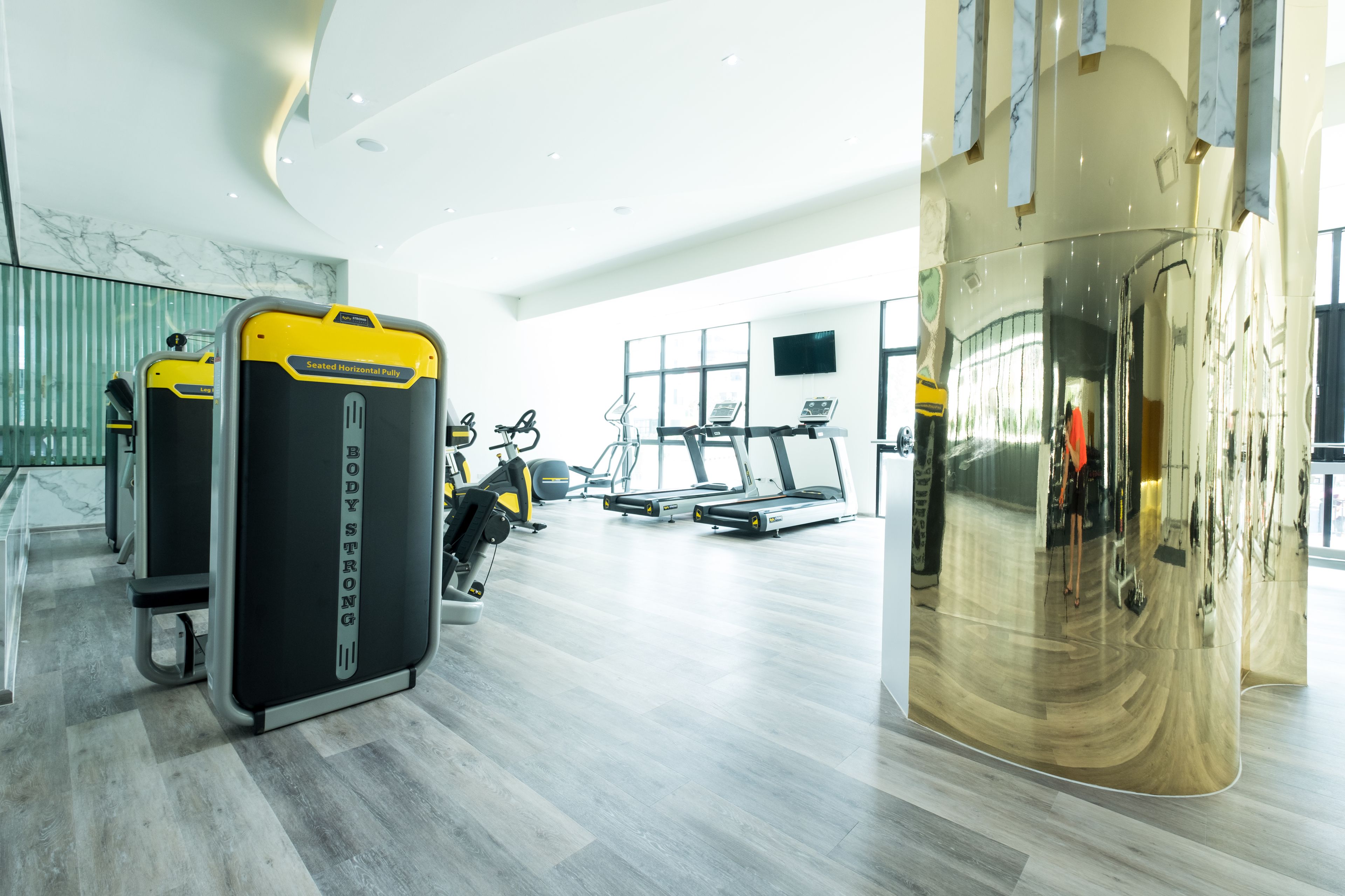 A modern gym with cardio machines, a treadmill, and a mirrored wall.