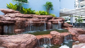 A rock waterfall feature with lush greenery and a modern building in the background. - P Plus Hotel (Pattaya)