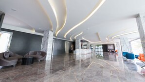 A modern lobby with marble floors, curved ceiling lights, and seating areas. - P Plus Hotel (Pattaya)
