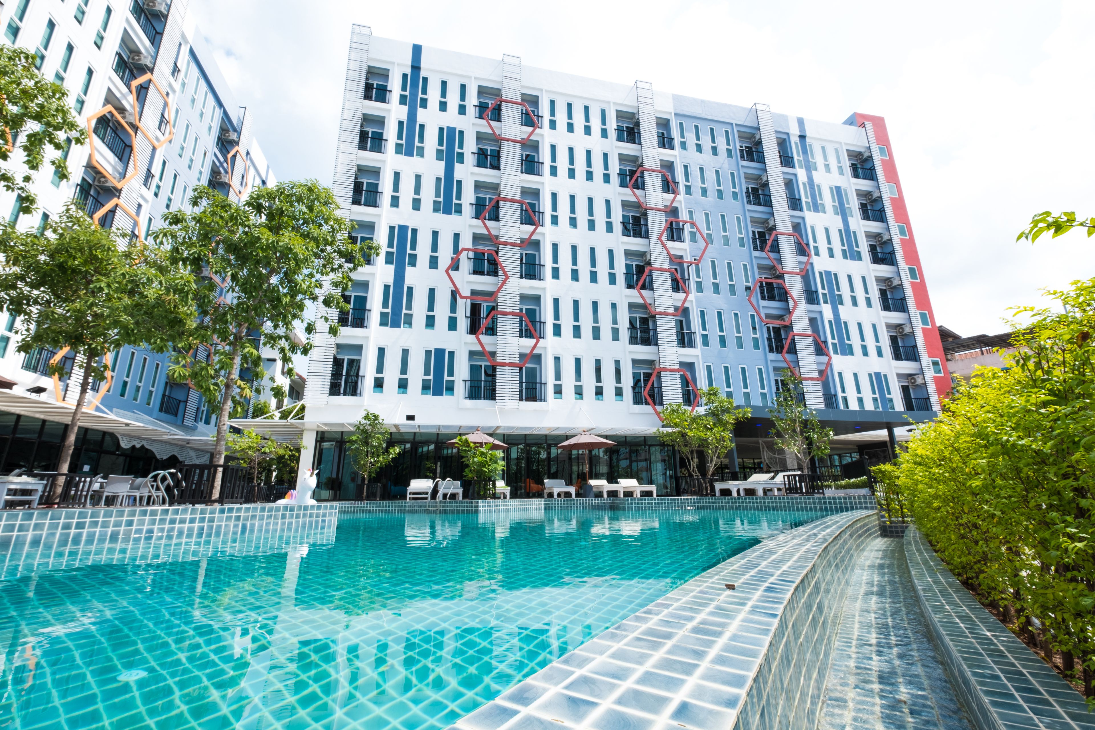 A modern hotel with a swimming pool, outdoor seating, and a large building with a distinctive hexagonal pattern on the facade.