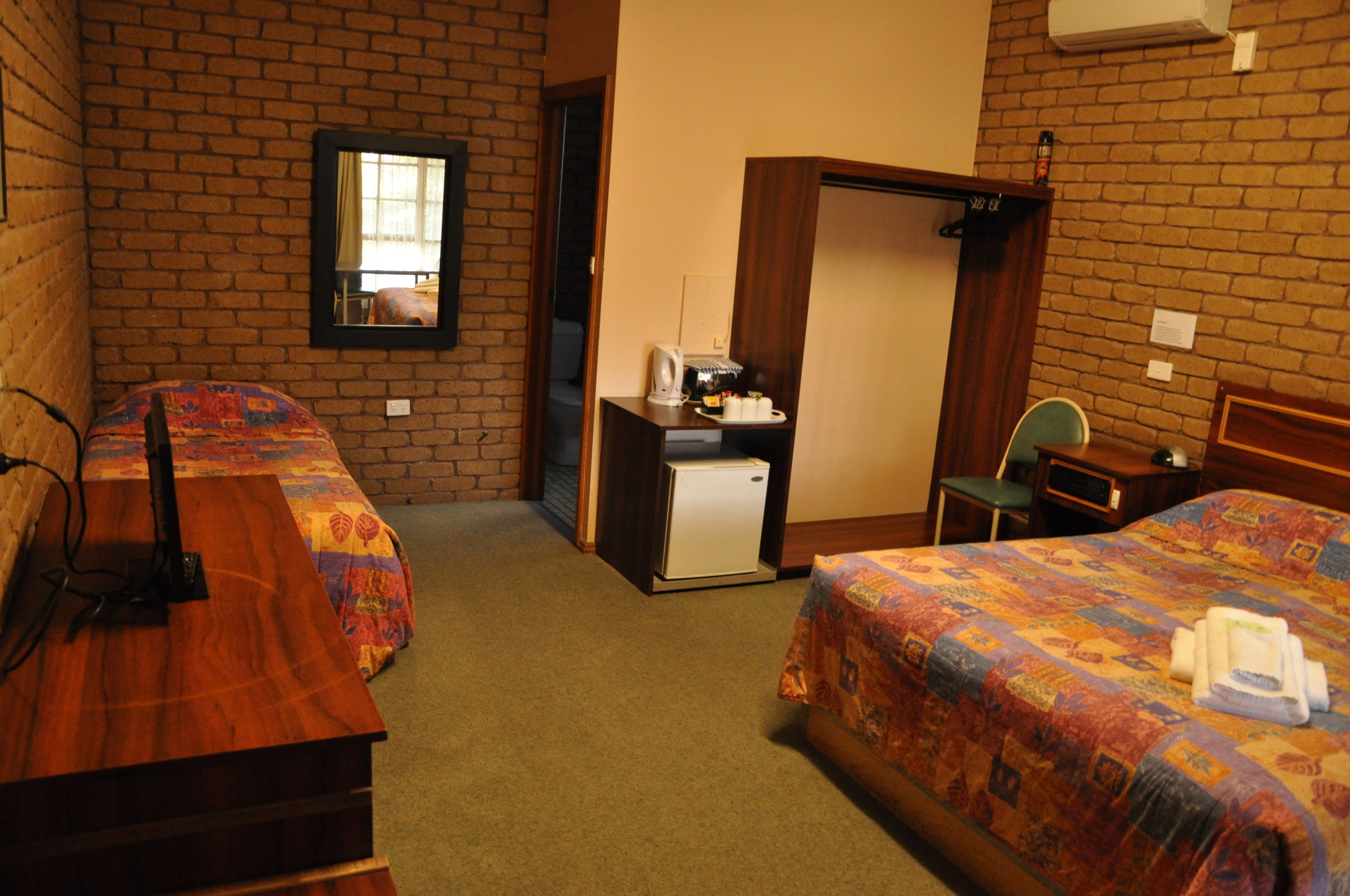 Ein Hotelzimmer mit zwei Betten, einem Schreibtisch inklusive Kühlschrank, einem Sessel und einem Spiegel an der Wand.