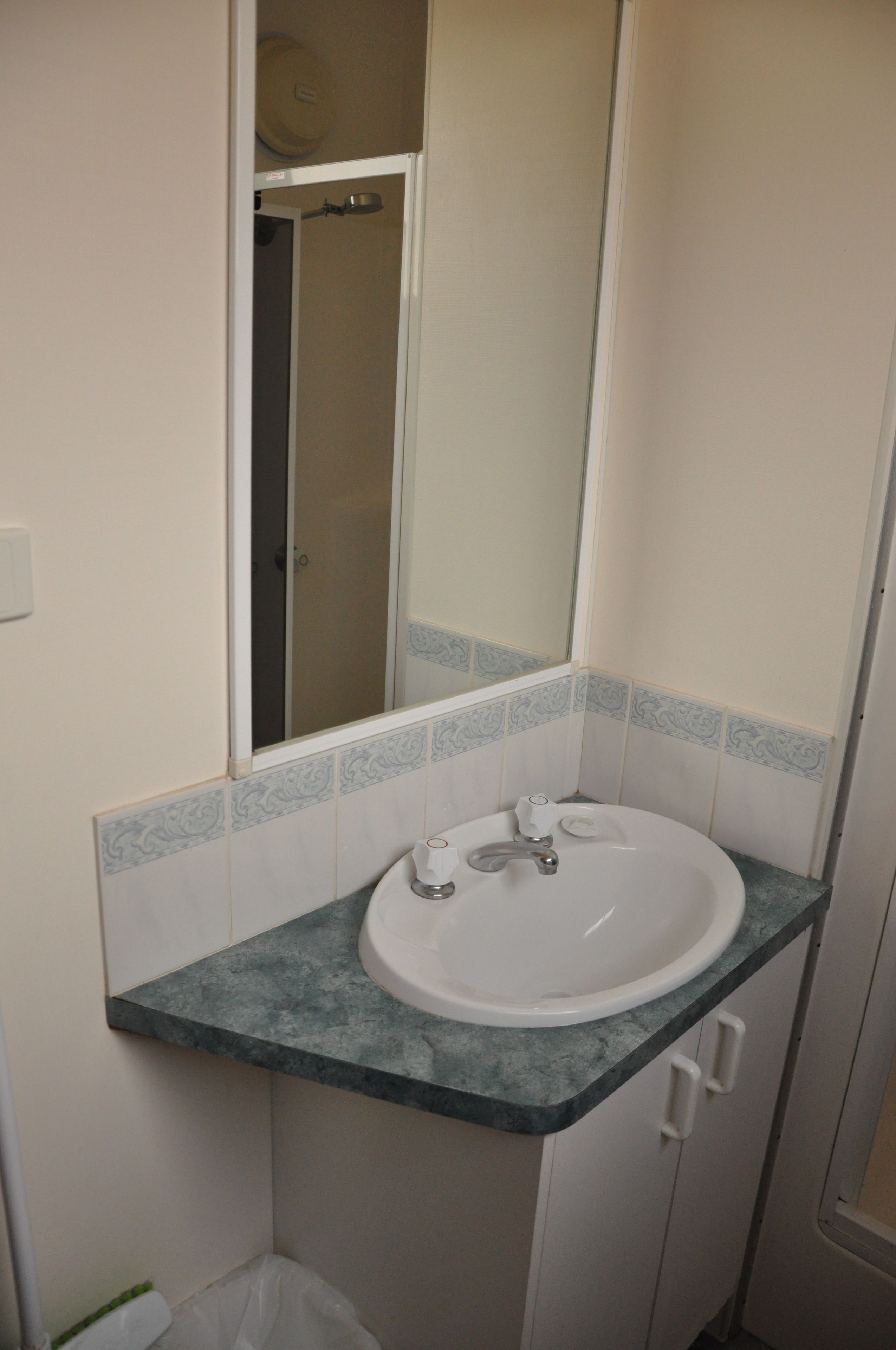 Une salle de bain avec un lavabo blanc, un miroir et une porte de douche.