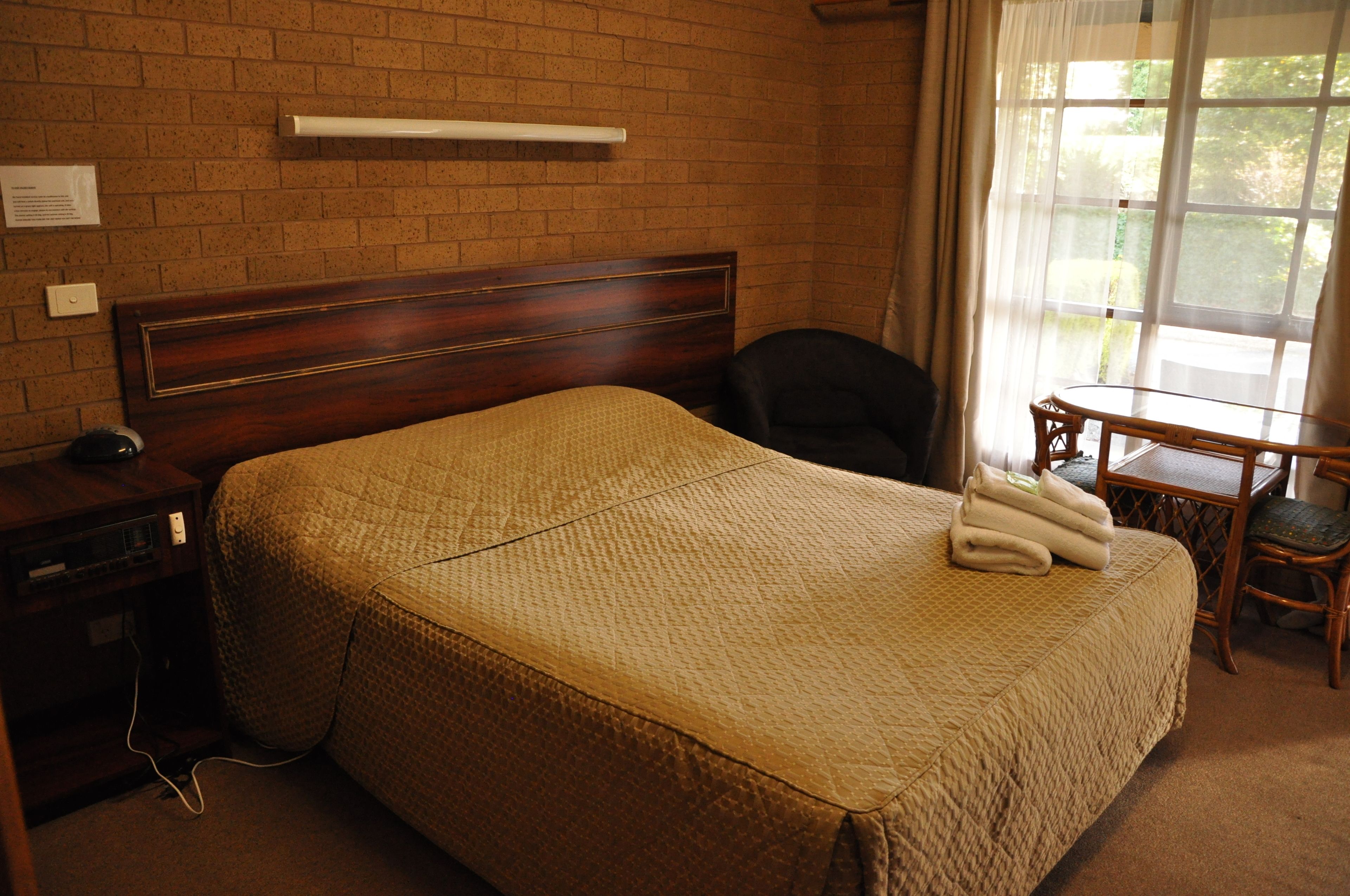 A hotel room with a large bed, a wooden headboard, a desk with a chair, and a window with curtains.