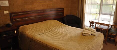 A hotel room with a large bed, a wooden headboard, a desk with a chair, and a window with curtains.