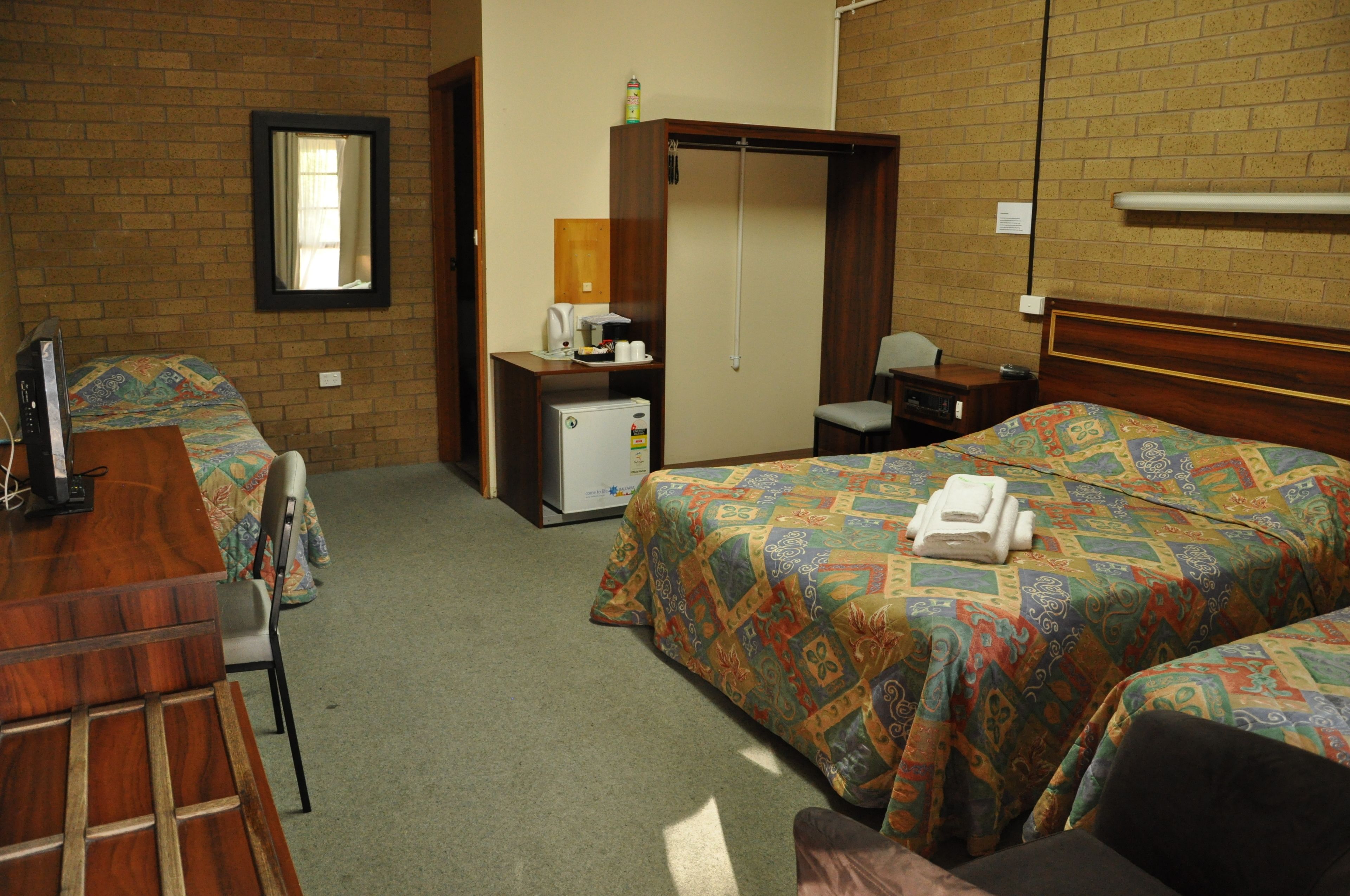 A hotel room with two beds, a desk, a chair, a small refrigerator, and a mirror on the wall.