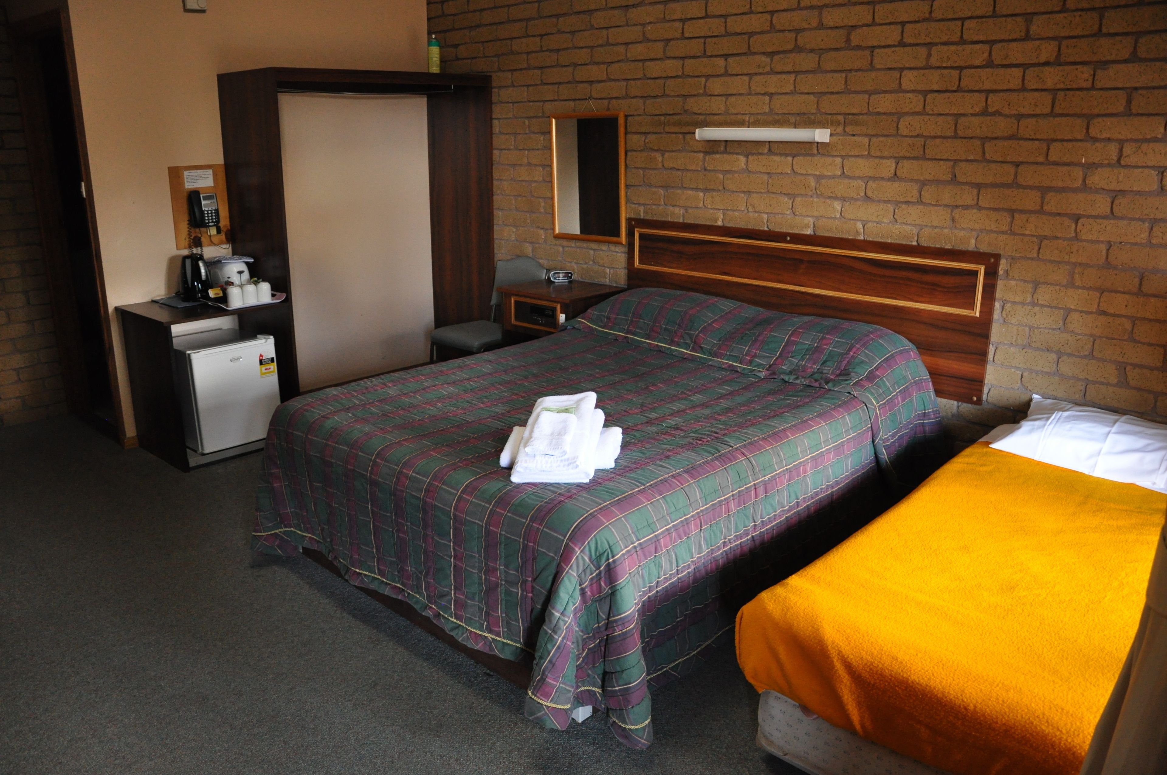 Habitación de hotel con cama, escritorio, teléfono, refrigerador y espejo sobre una pared de ladrillo.