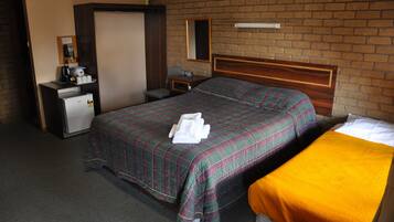 Habitación de hotel con cama, escritorio, teléfono, refrigerador y espejo sobre una pared de ladrillo.