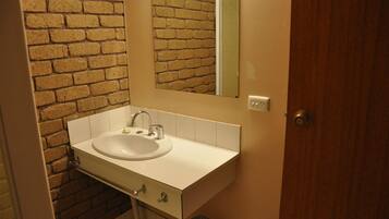A bathroom with a white sink, a mirror, and a brick wall.