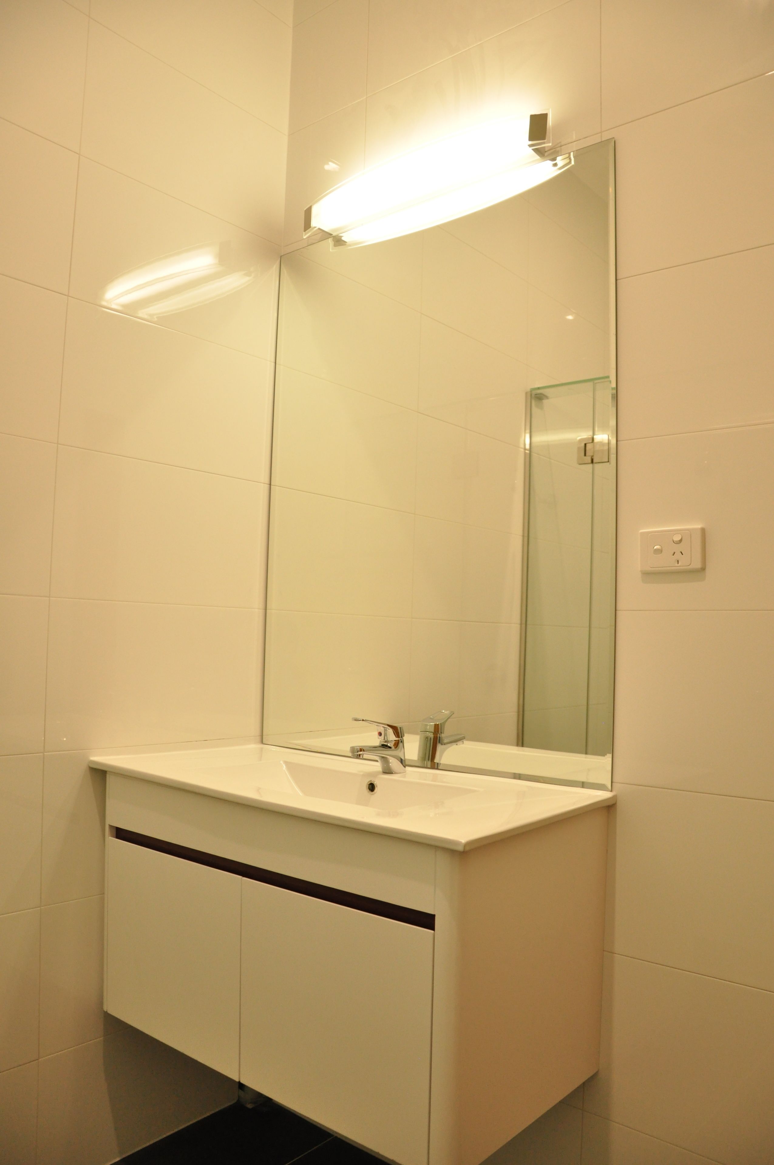 Een badkamer met een wit wastafelmeubel, spiegel en kast.