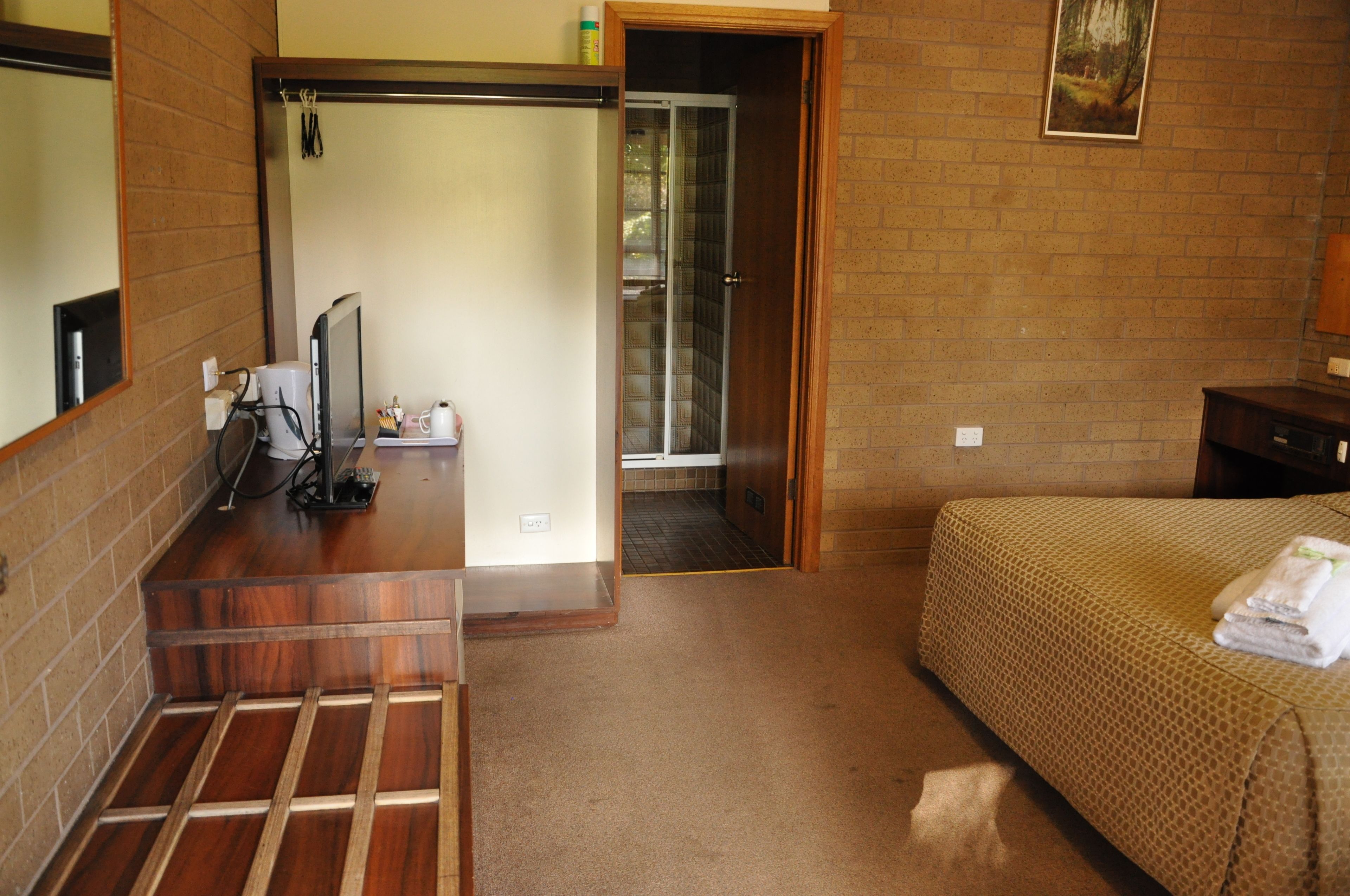 A hotel room with a bed, a desk with a computer, a shower, and a painting on the wall.
