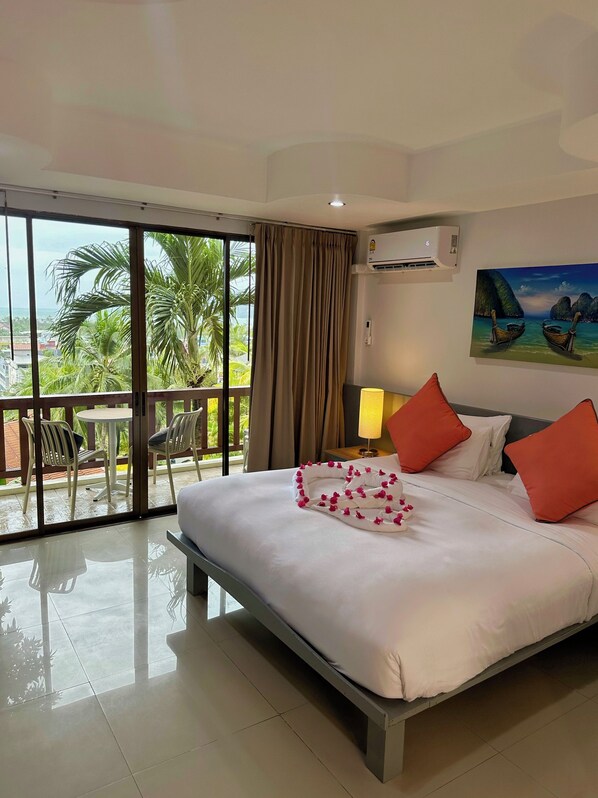 A hotel room with a large bed, a balcony with chairs, and a painting of boats. - Sea Hills Resort (Patong)