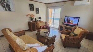 A living room with wicker furniture, a glass coffee table, and a television. - Baansiesom Private Pool Villa (Pranburi)