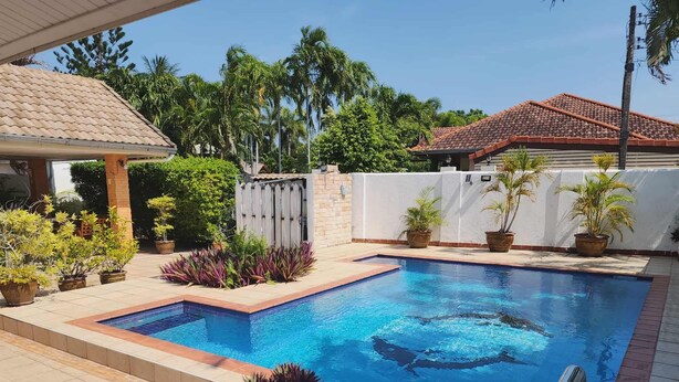 A swimming pool with a tiled deck, surrounded by potted plants and a white wall. - Baansiesom Private Pool Villa (Pranburi)