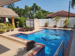 A swimming pool with a tiled deck, surrounded by potted plants and a white wall. - Baansiesom Private Pool Villa (Pranburi)