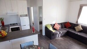Eine moderne Küche mit weißen Schränken, ein Essbereich mit Tisch und Stühlen sowie ein graues Ecksofa mit roten und beigen Kissen.
