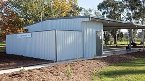 Ein Gebäude aus Metall mit überdachter Veranda, umgeben von Bäumen und einer Rasenfläche.
