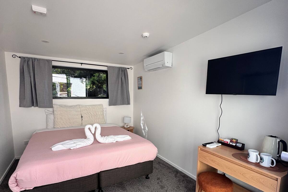 A hotel room with a bed, a desk, a television, and an air conditioning unit.