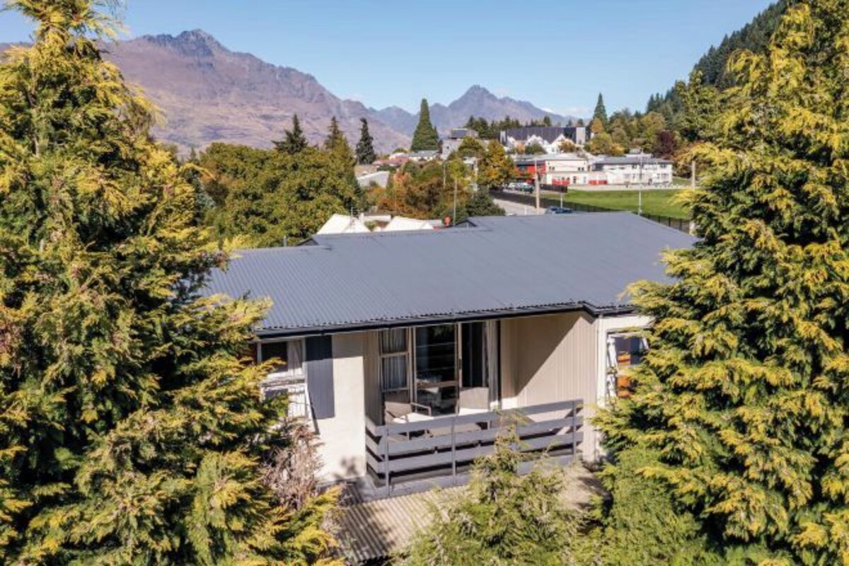 A modern house with a flat roof, surrounded by trees and mountains in the background.
