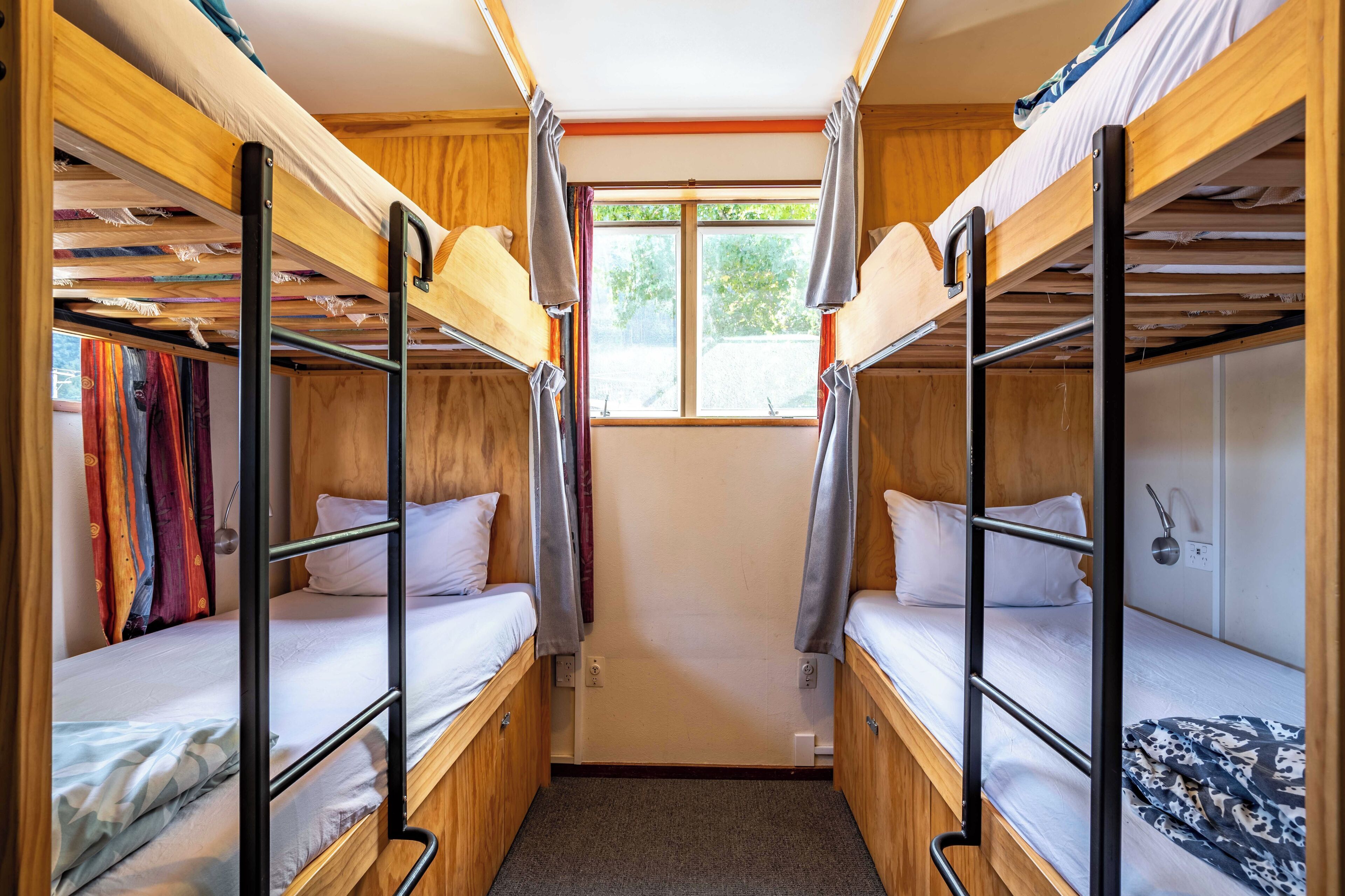 Une petite chambre avec des lits superposés, une fenêtre avec des rideaux et une petite table de chevet.