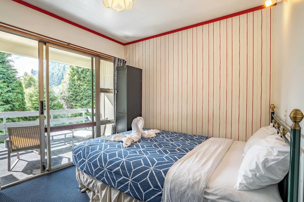 A hotel room with a large bed, a sliding glass door leading to a balcony, and a view of trees.