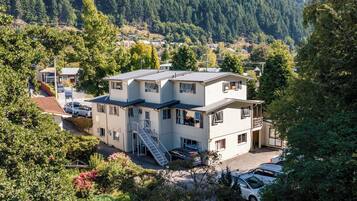 A multi-story building with a staircase leading to the entrance, surrounded by lush greenery and a forested hillside.