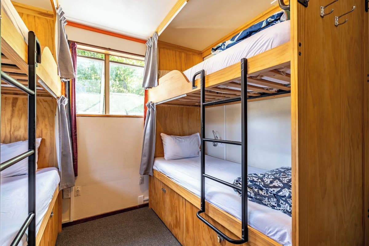 A compact, well-lit room with bunk beds, a window with curtains, and a door with hooks.