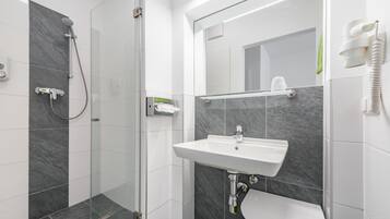 A modern bathroom with a glass-enclosed shower, a white sink, and a marble-tiled wall.