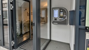 A self-check-in/out kiosk at a hotel entrance with a 24/7 service sign. - Hotel City Rooms Wels (Wels)