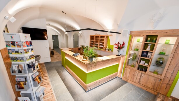 A reception area with a green counter, a wooden display cabinet, and a plant. - Hotel City Rooms Wels (Wels)