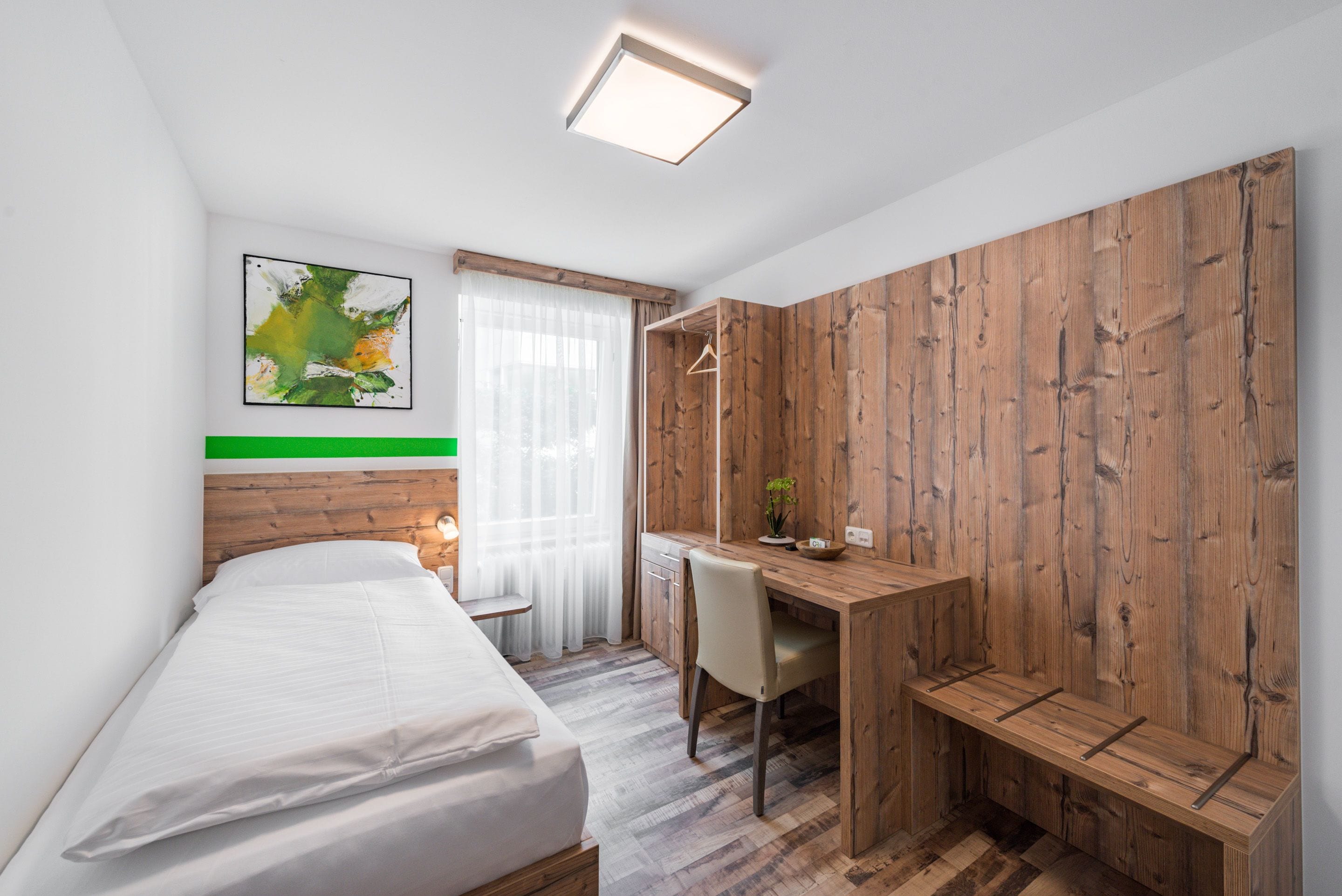 A hotel room with a bed, a desk, and a wooden wardrobe.