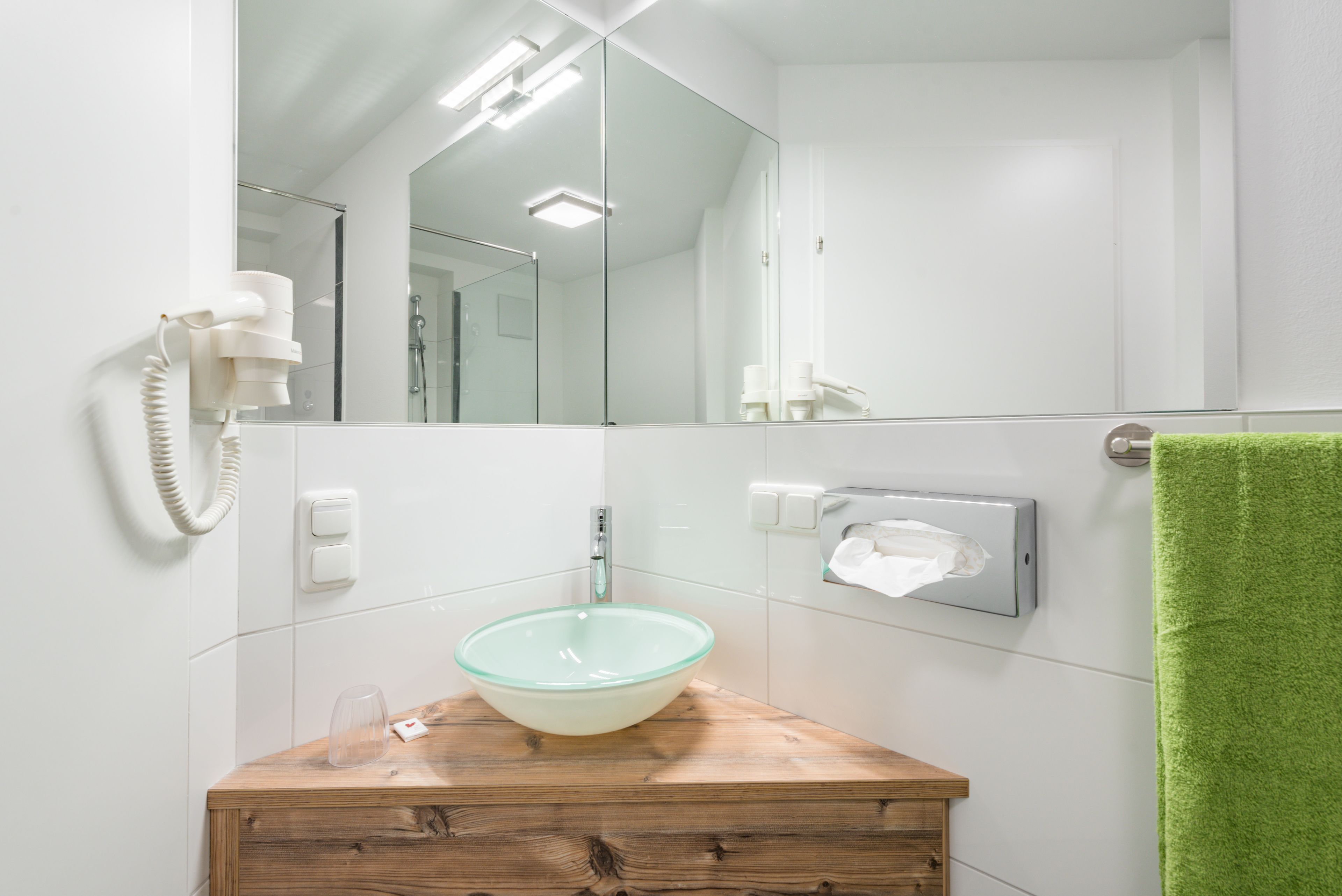 A bathroom with a glass bowl sink, wooden vanity, a mirror, a green towel, and a telephone.