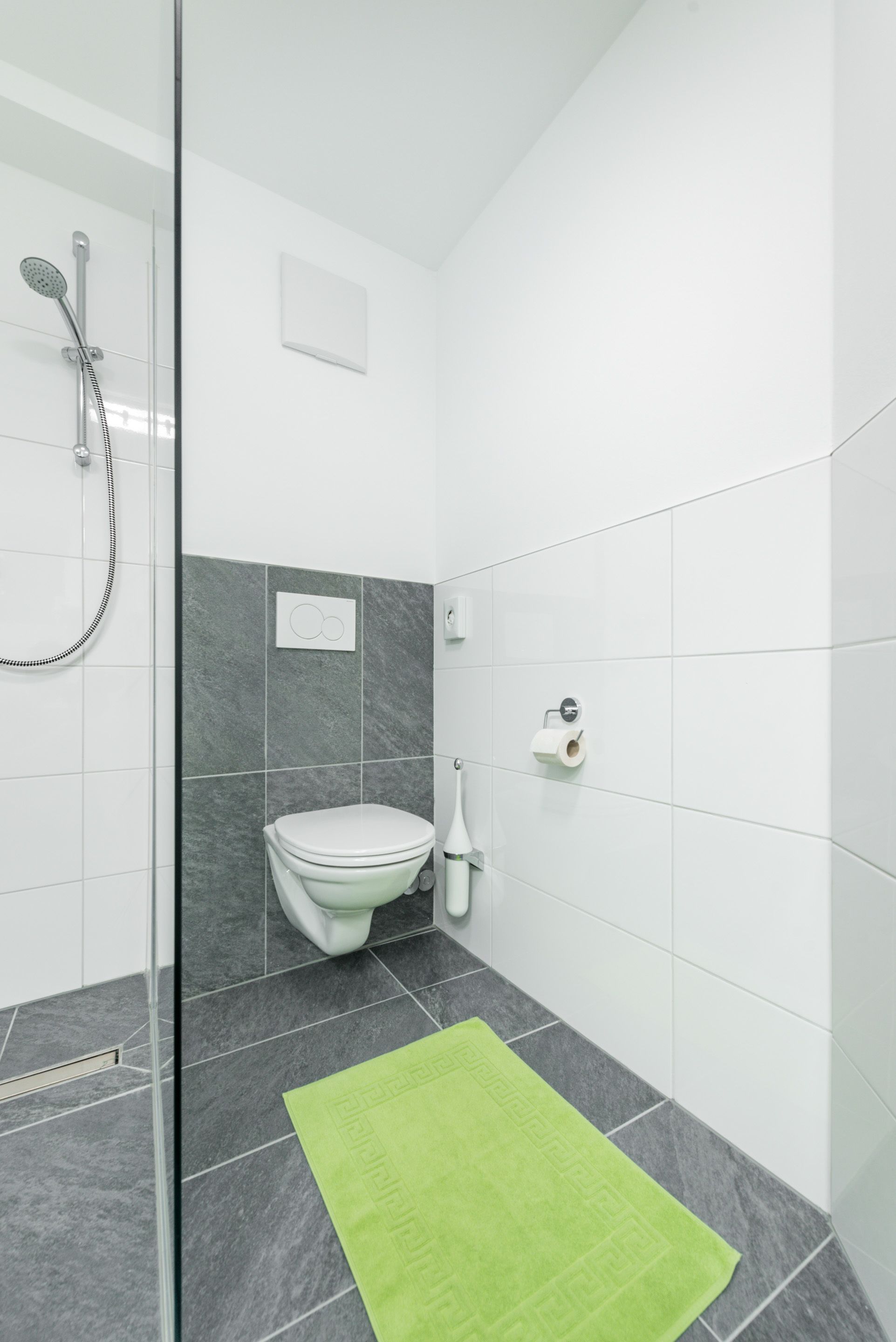 A modern bathroom with a glass shower enclosure, a toilet, and a green towel on the floor.