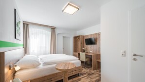 A hotel room with a bed, a desk, a chair, a small table, and a TV. - Hotel City Rooms Wels (Wels)