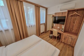 Una habitación de hotel con una cama, un escritorio con una silla, un televisor y un armario de madera.