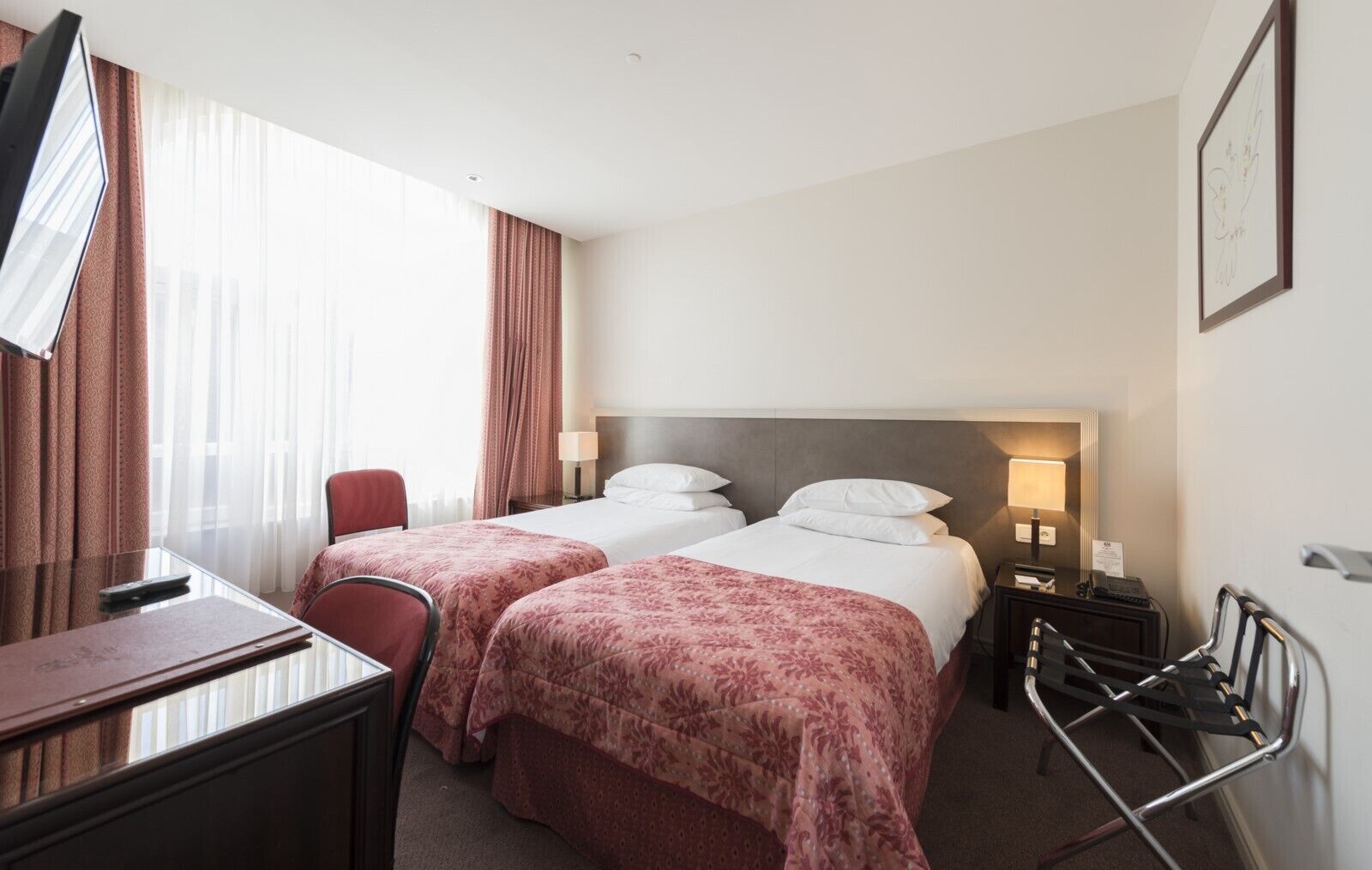 Une chambre d’hôtel avec deux lits, un bureau, une chaise, une télévision et une fenêtre avec des rideaux.