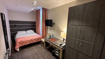 Habitación de hotel con cama, escritorio, silla, armario y televisor montado en la pared.
