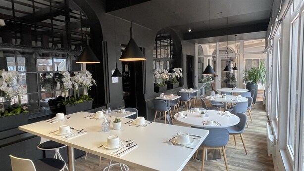 Un espace de restauration moderne avec des tables et des chaises rondes, une décoration de table blanche et des luminaires suspendus noirs.