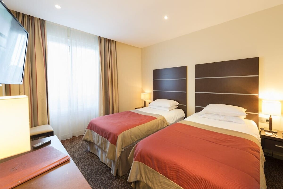 Une chambre d’hôtel avec deux lits, une télévision, un bureau et une chaise.