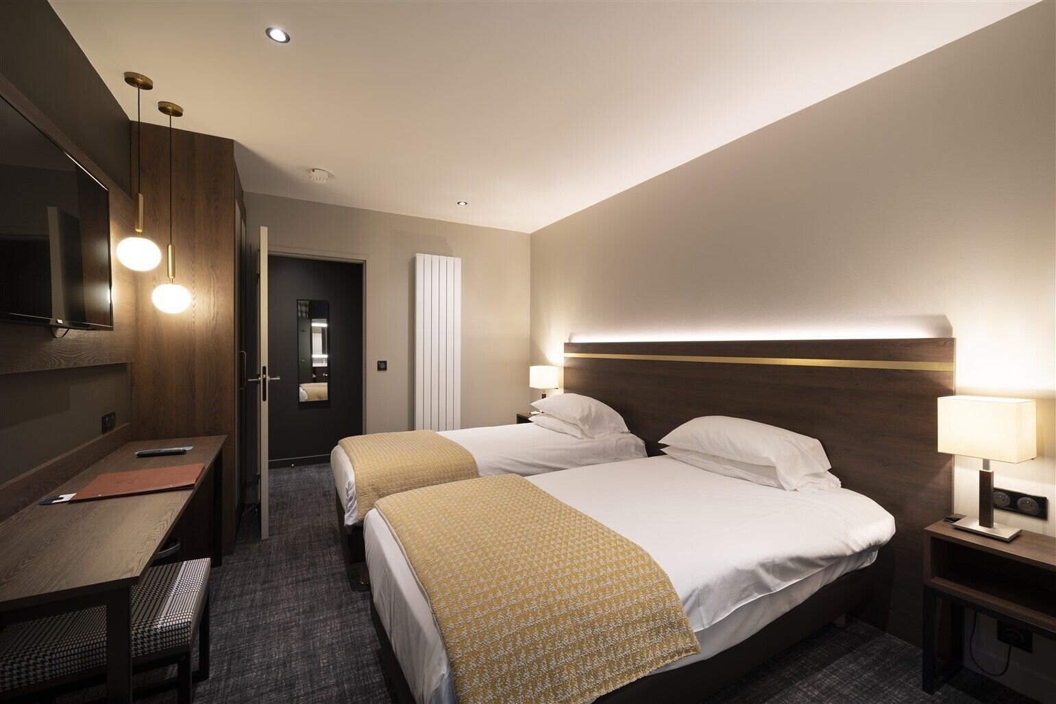 A hotel room with two beds, a desk, a mirror, and a TV.