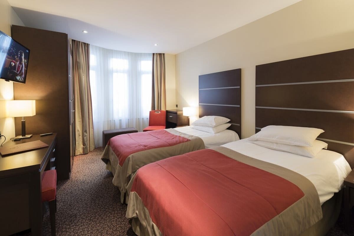 Une chambre d’hôtel avec deux lits, un bureau, une télévision et une fenêtre avec des rideaux.