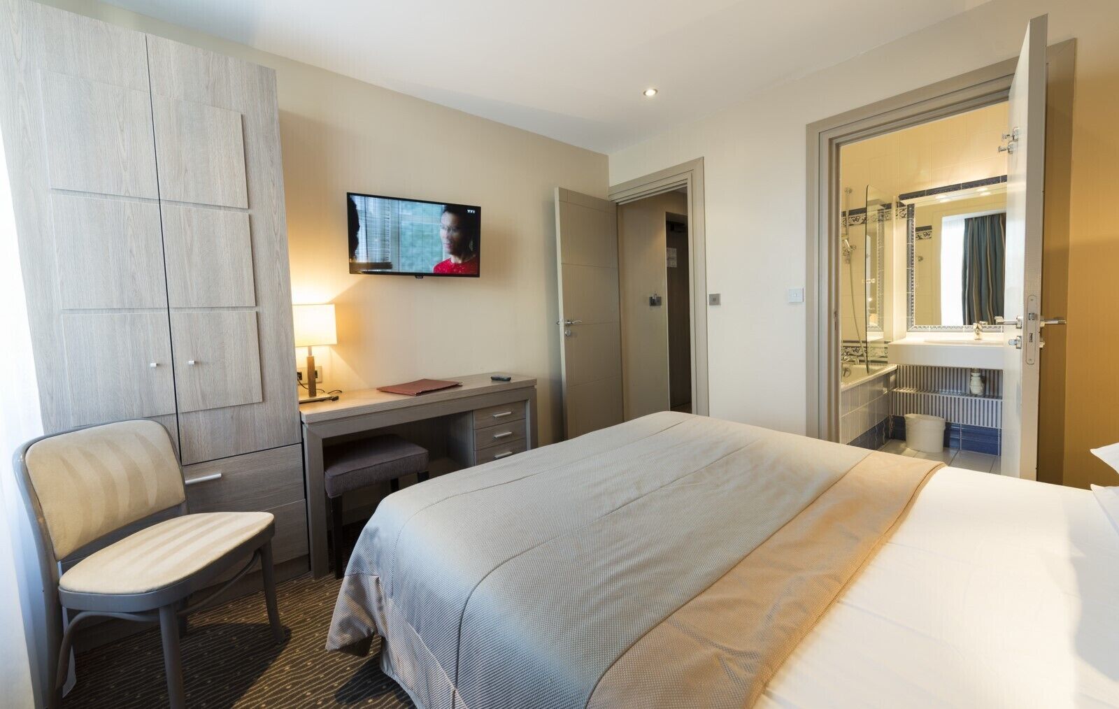 Een hotelkamer met een bed, een bureau met stoel, een televisie, een kledingkast en een badkamer.