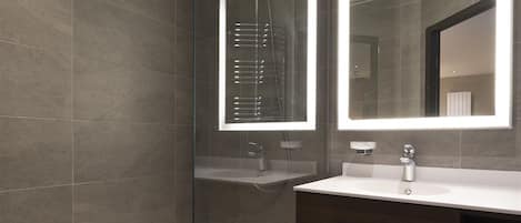 Un baño moderno con ducha envuelta en vidrio, un espejo grande y un tocador de madera oscura.