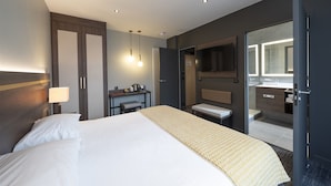 Une chambre d’hôtel moderne avec un grand lit, une table de chevet, une lampe et une salle de bain équipée d’un miroir et d’un lavabo.