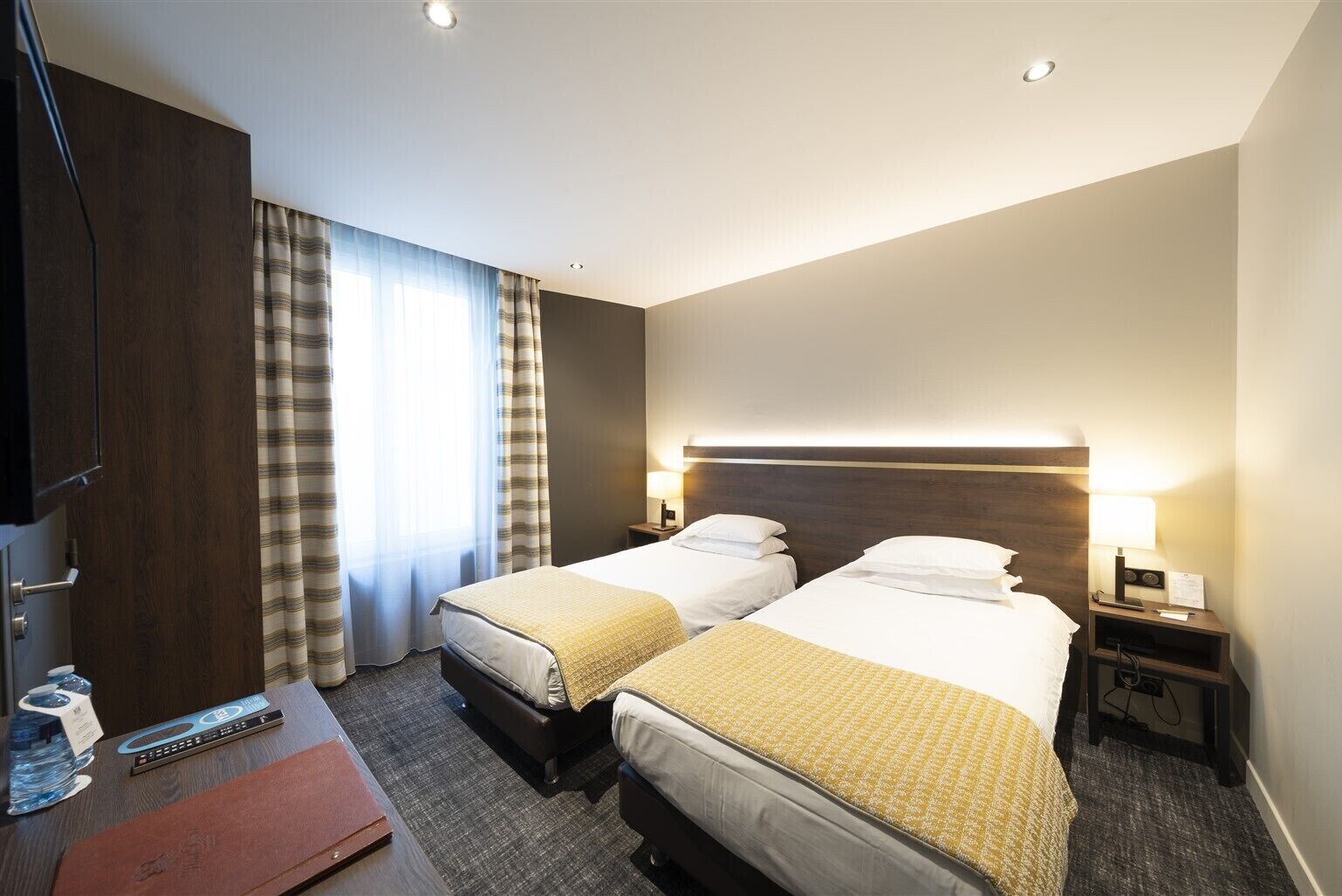 Habitación de hotel con dos camas, un escritorio, un televisor y una ventana con cortinas.