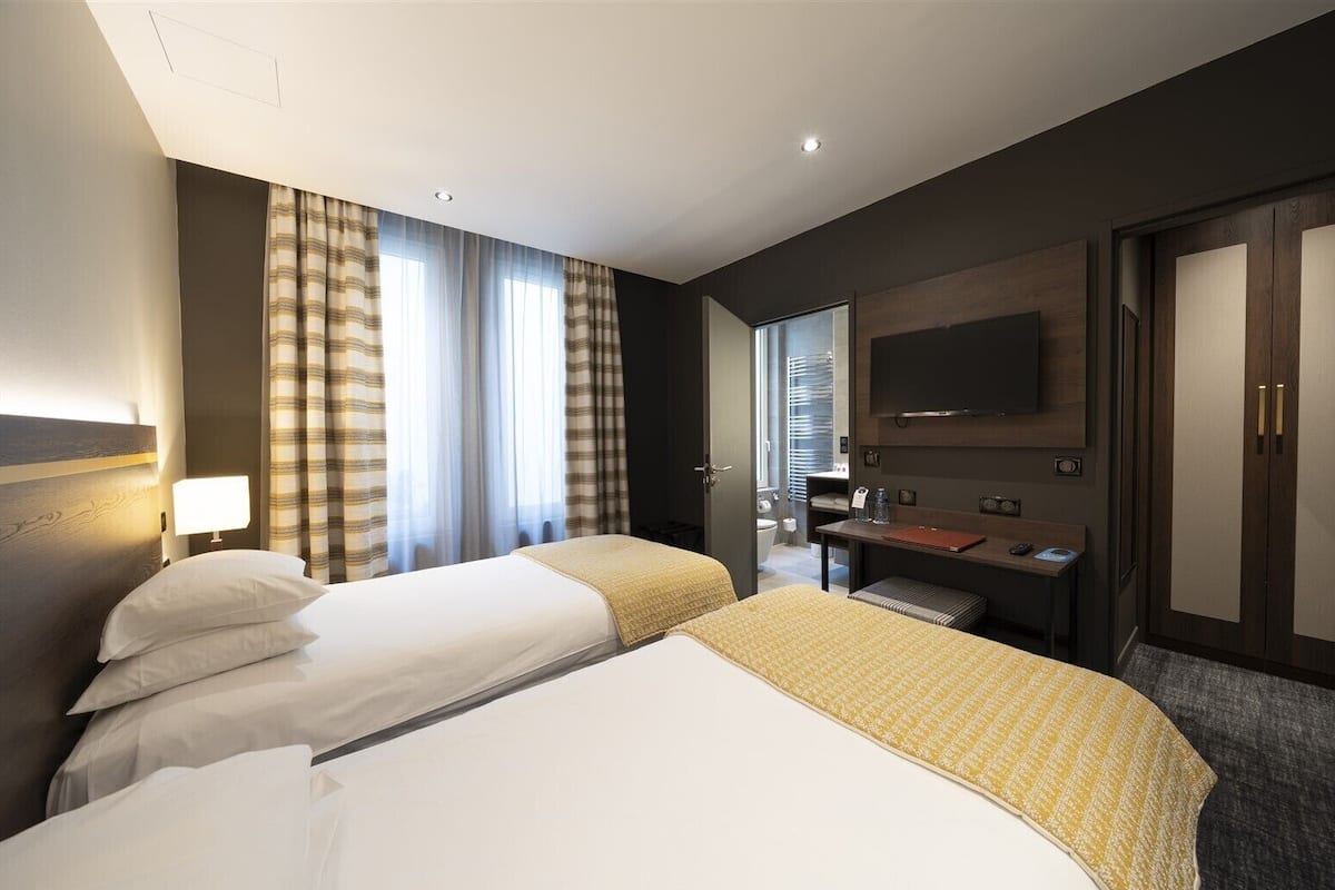 Une chambre d’hôtel avec deux lits, un bureau, une télévision et une armoire.