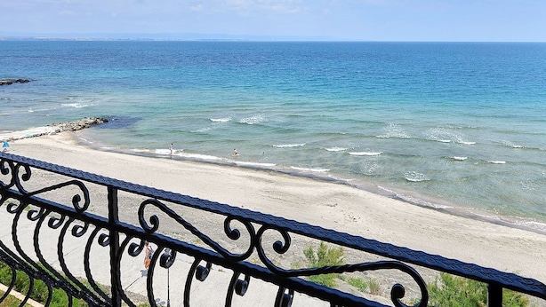 Une plage avec une eau d’un bleu limpide, un rivage sablonneux et une rambarde métallique au premier plan.